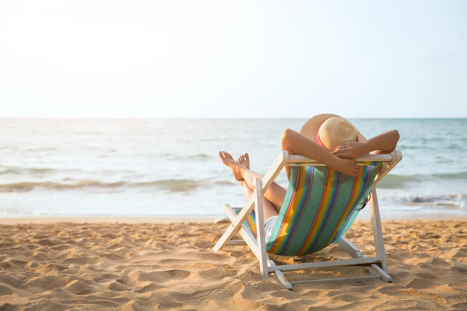 A woman sitting back and relaxing in a striped deckchair on a sunny beach, laptop closed beside her