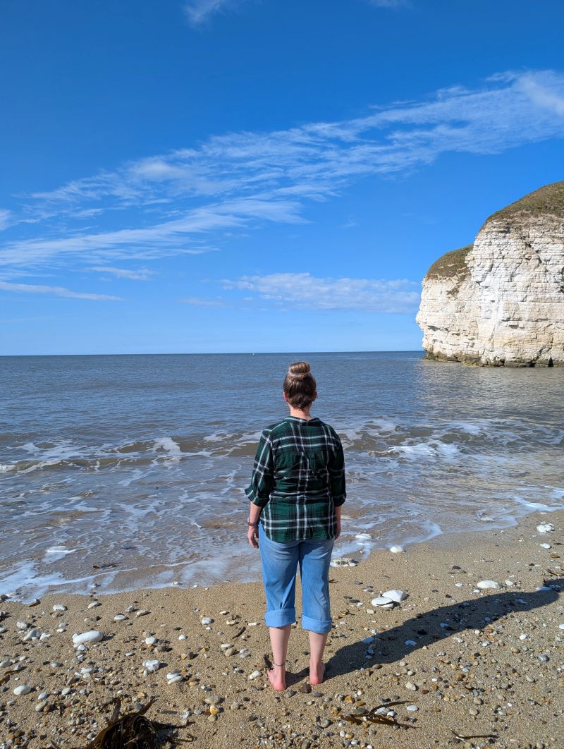 Woman standing barefoot on a Yorkshire beach looking out to sea, with chalk cliffs in the background